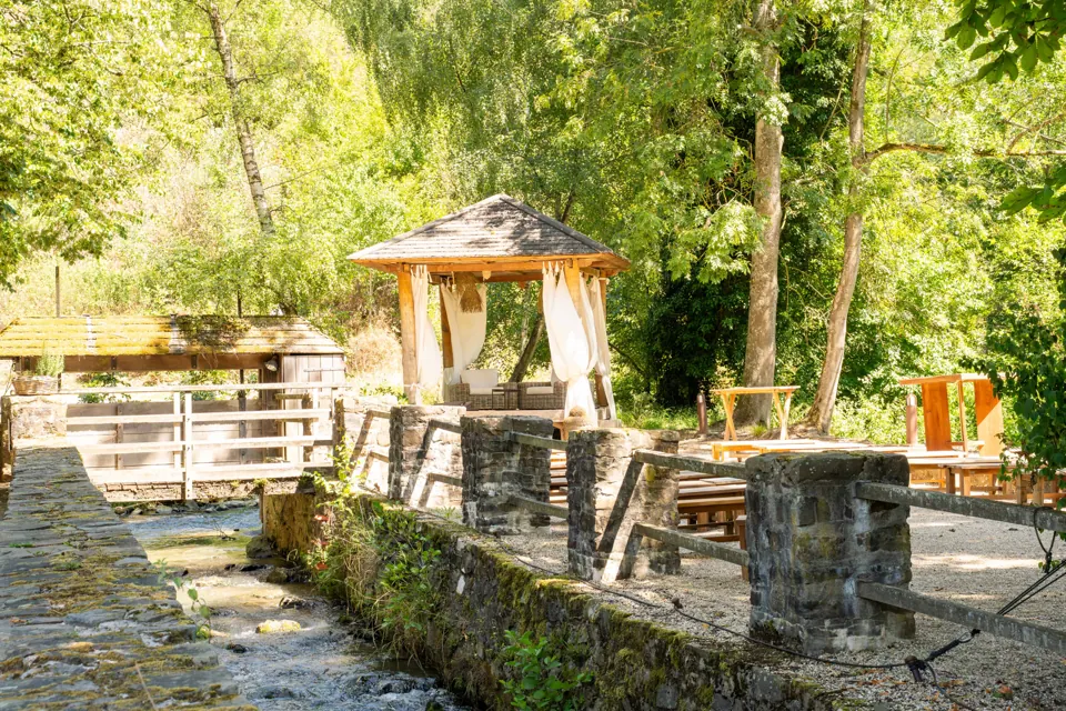 Gazebo mit weißen Vorhängen für freie Trauungen am Bachlauf der Auermühle