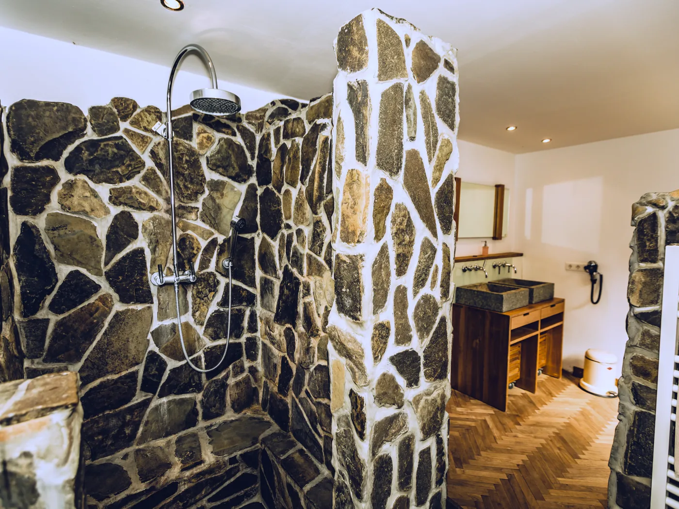Bad mit Natursteinwand und Fischgrätparkett im Gästehaus der Auermühle