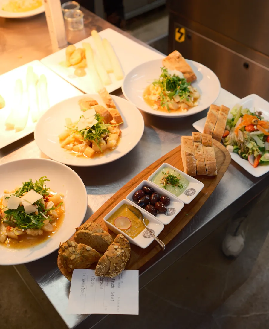 Angerichtete Teller aus der Küche: Spargelsalat, Brotzeitbrett mit Dips und Oliven