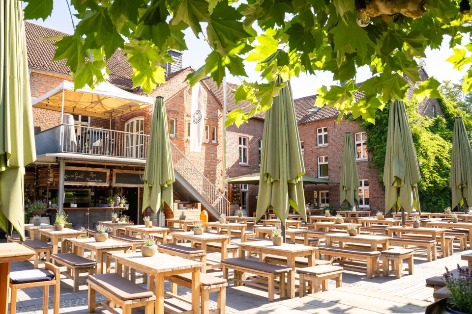 Sonniger Biergarten mit Holztischen im Innenhof der Auermühle in Ratingen